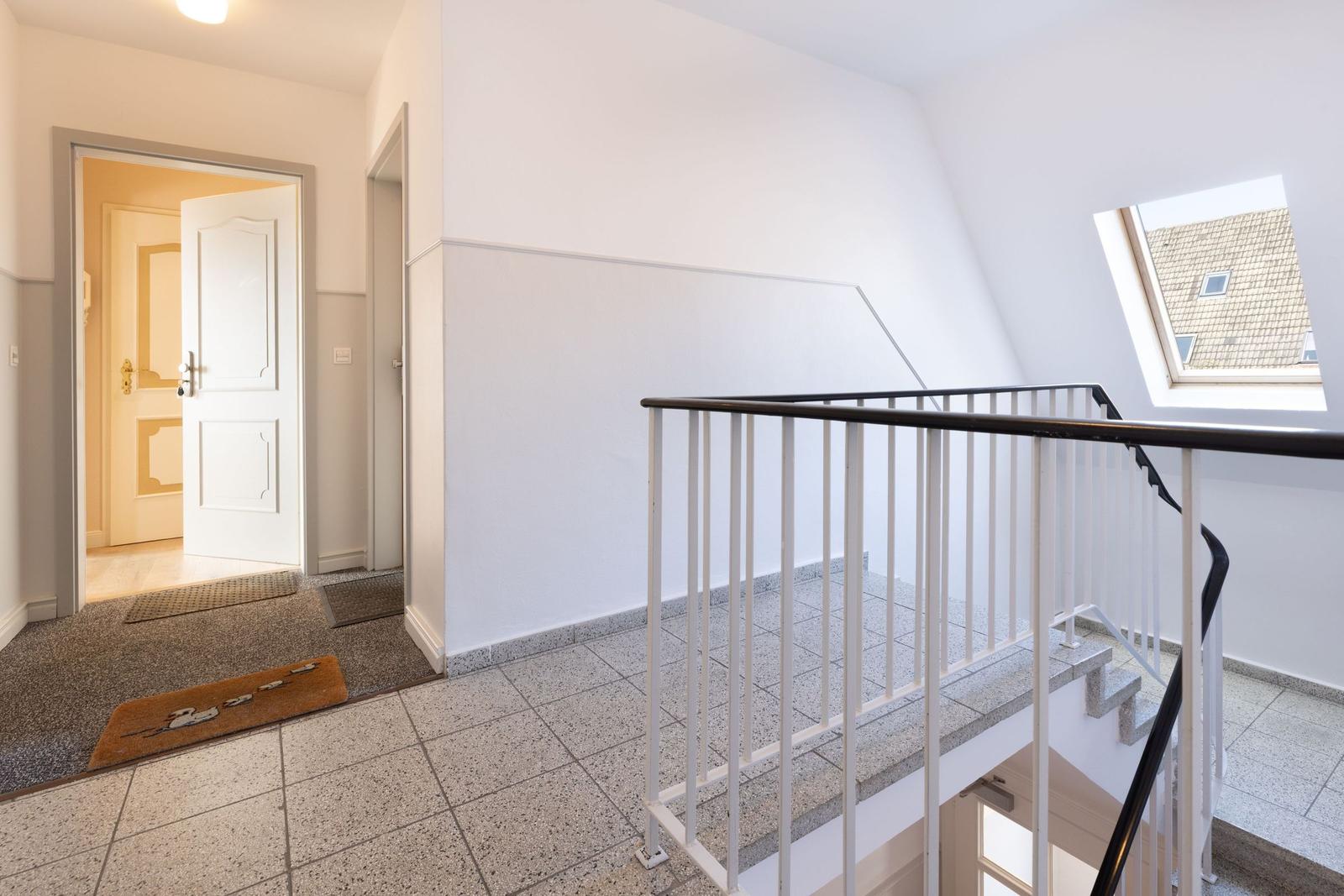 Eingangsbereich mit Treppenhaus und Dachfenster. Weiße Wände und Terrazzoboden.