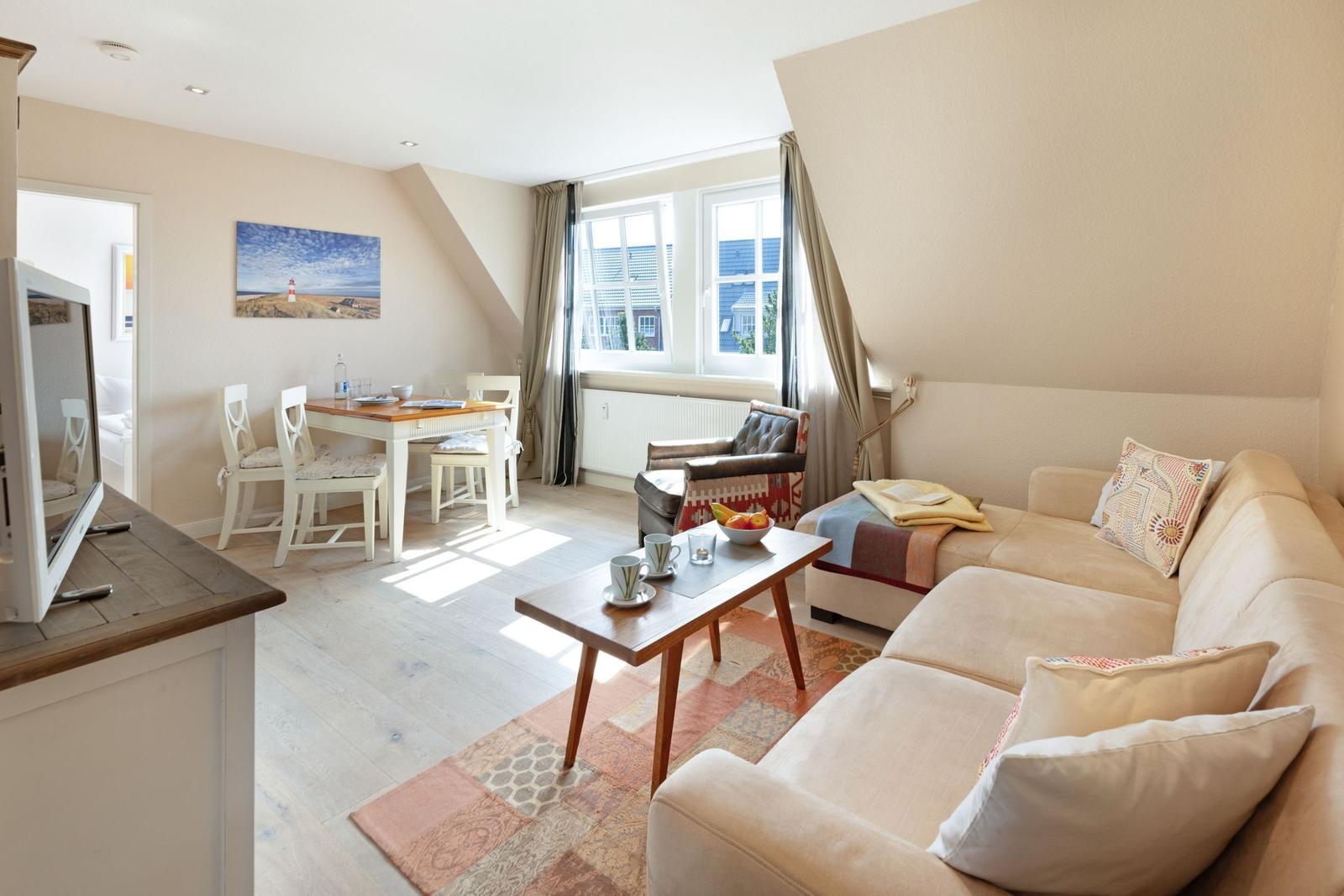 Wohn- und Essbereich mit Sofa, Tisch und Stühlen. Fenster mit Blick nach draußen.