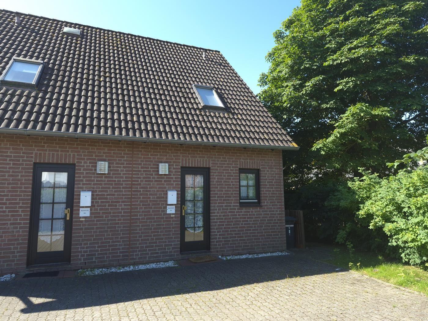 Ein zweistöckiges Haus mit rotem Ziegelmauerwerk und Dachfenstern. Vorderseite mit zwei Türen und einem Fenster.