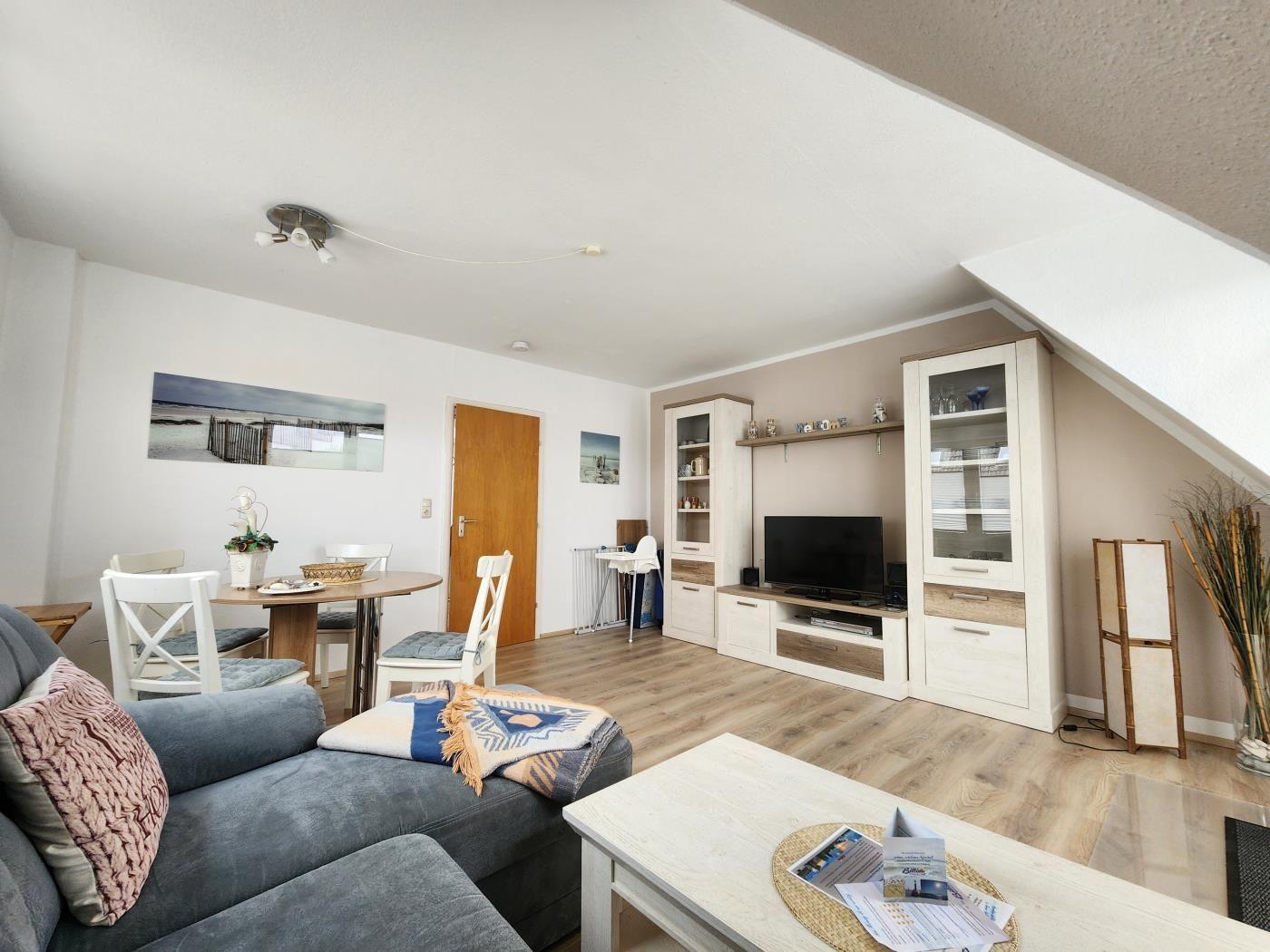 Wohnzimmer mit Sofa, Esstisch, Fernseher und Schrank. Holzfußboden und Dachschräge.