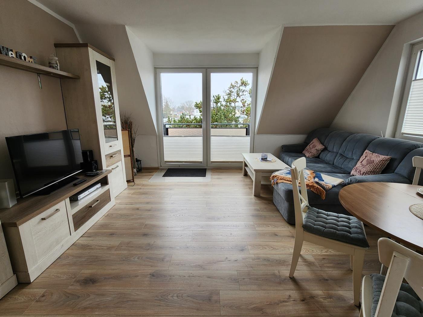 Wohnzimmer mit Sofa, Fernseher und Balkonzugang.