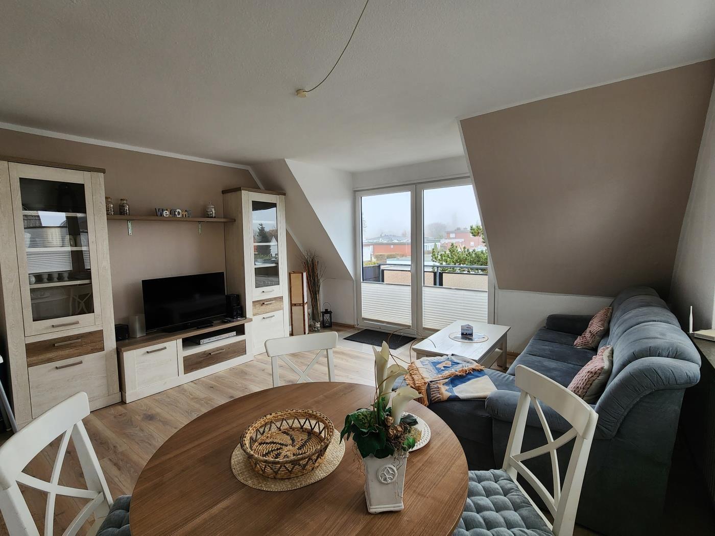 Wohn- und Essbereich mit Sofa, TV und Balkonansicht.