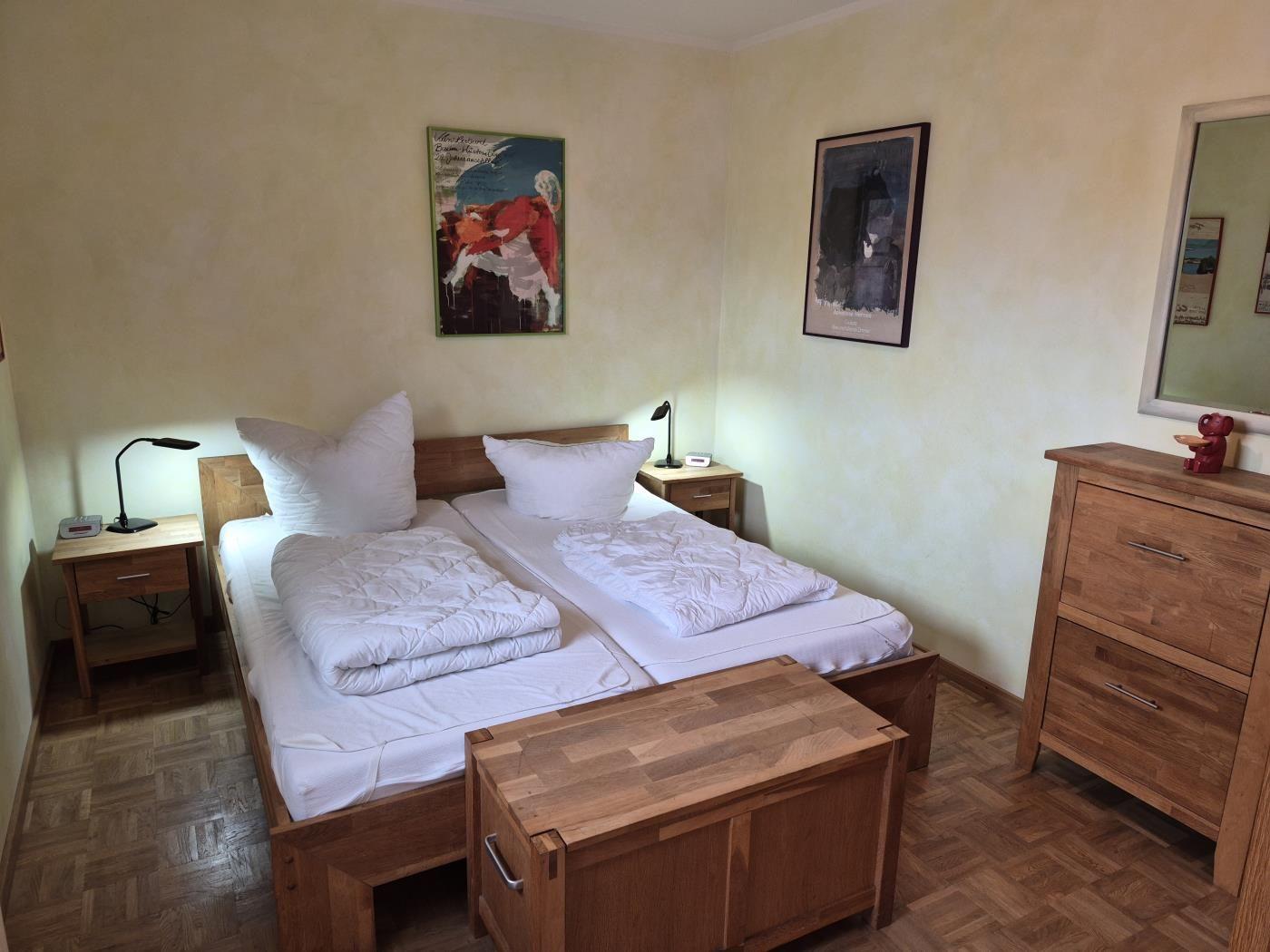 Zimmer mit Doppelbett, zwei Nachttischen und Holzmöbeln. Wandbilder und Spiegel sind vorhanden.