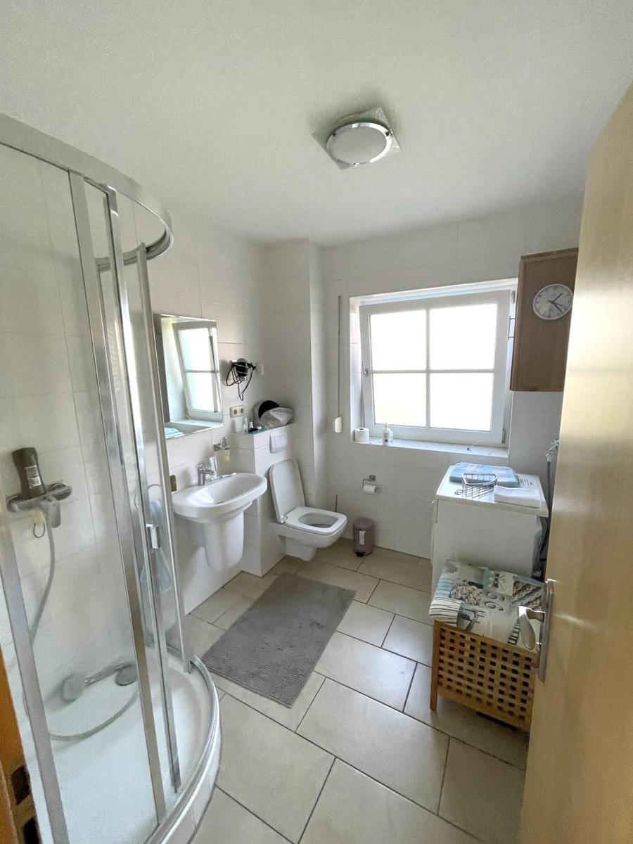 Badezimmer mit Dusche, Waschbecken, Toilette und Fenster.