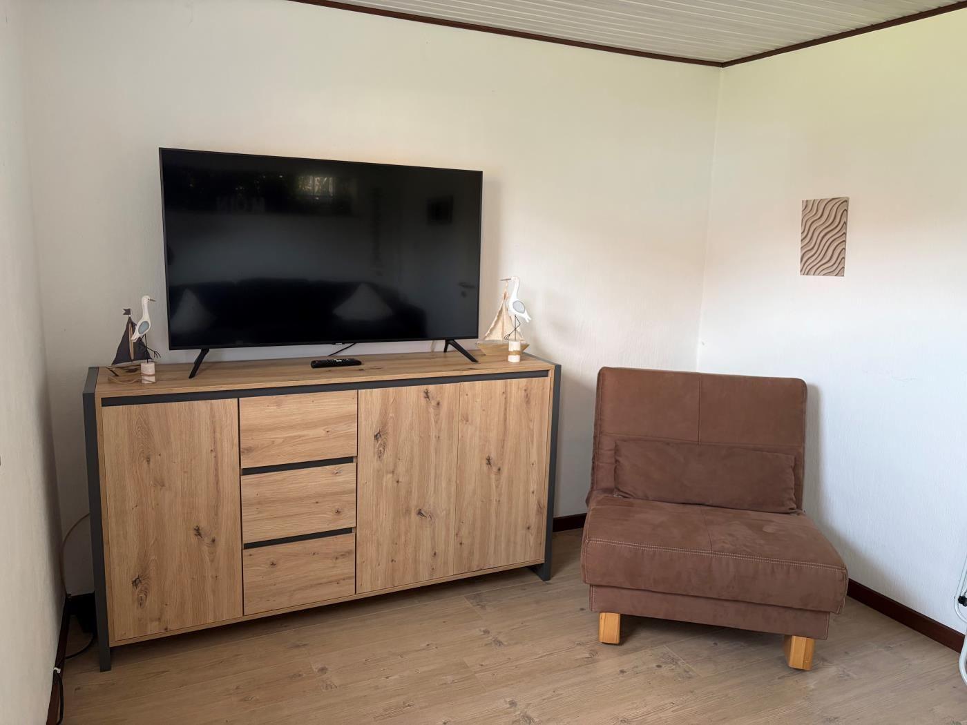 Ein Raum mit Fernseher auf einem Holzschrank und einem braunen Sessel.