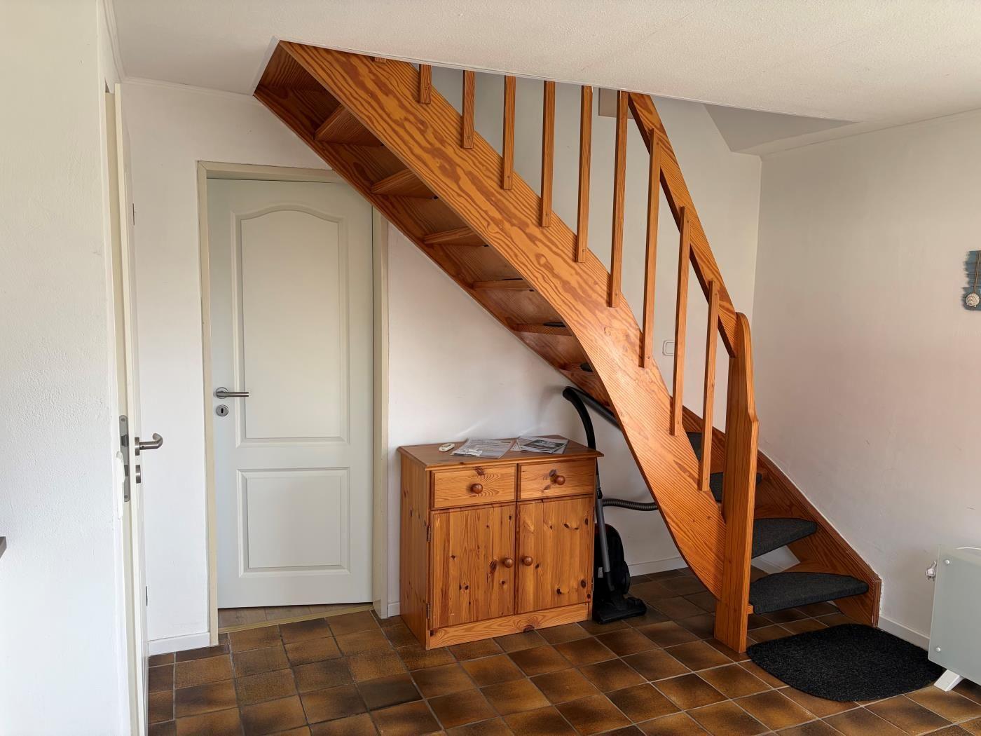 Holztreppe führt nach oben, daneben steht ein Holzschrank mit Schubladen und Türen.