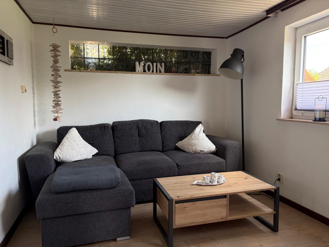 Ein Wohnzimmer mit grauem Sofa, Holztisch und Fenster mit Jalousie.