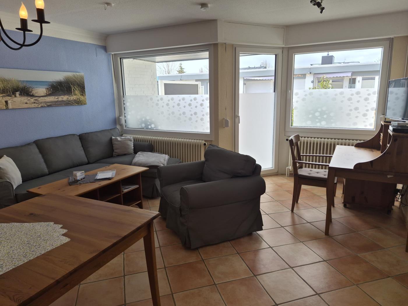 Wohnzimmer mit Sofa, Sessel und Esstisch. Durchgänge zu Balkon und Garten.