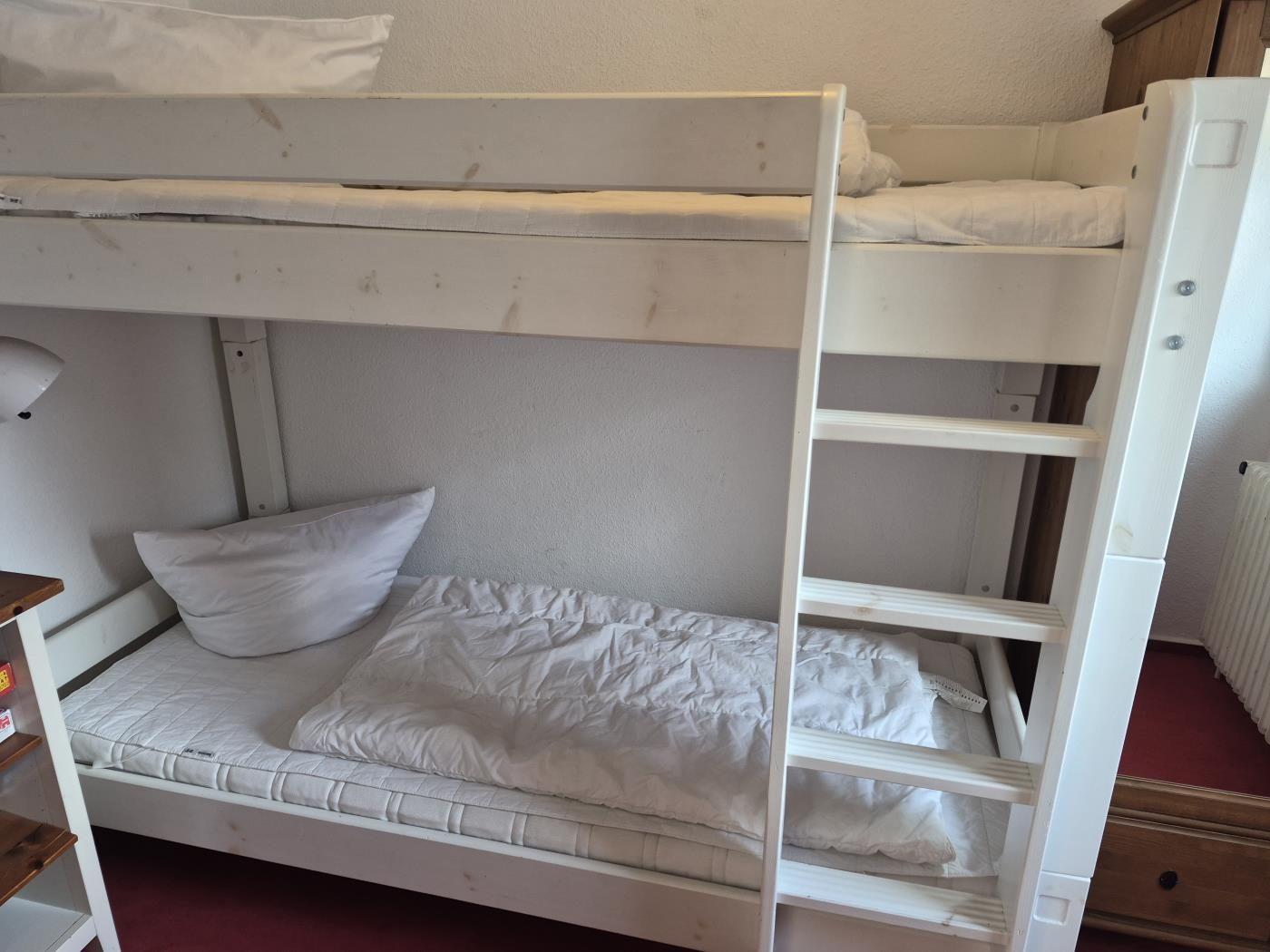 Ein weißes Doppelstockbett mit Matratzen und Kissen.