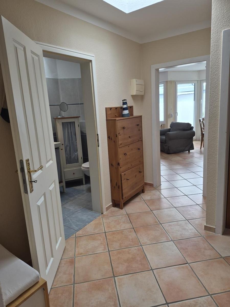 Flur mit Holzschrank, Tür zu Bad und Blick in Wohnzimmer mit Sessel.