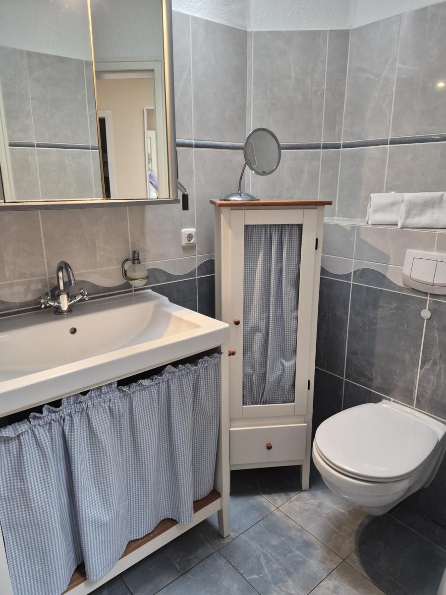 Bad mit Waschbecken, Spiegel, WC und Schrank mit Gittertüren.
