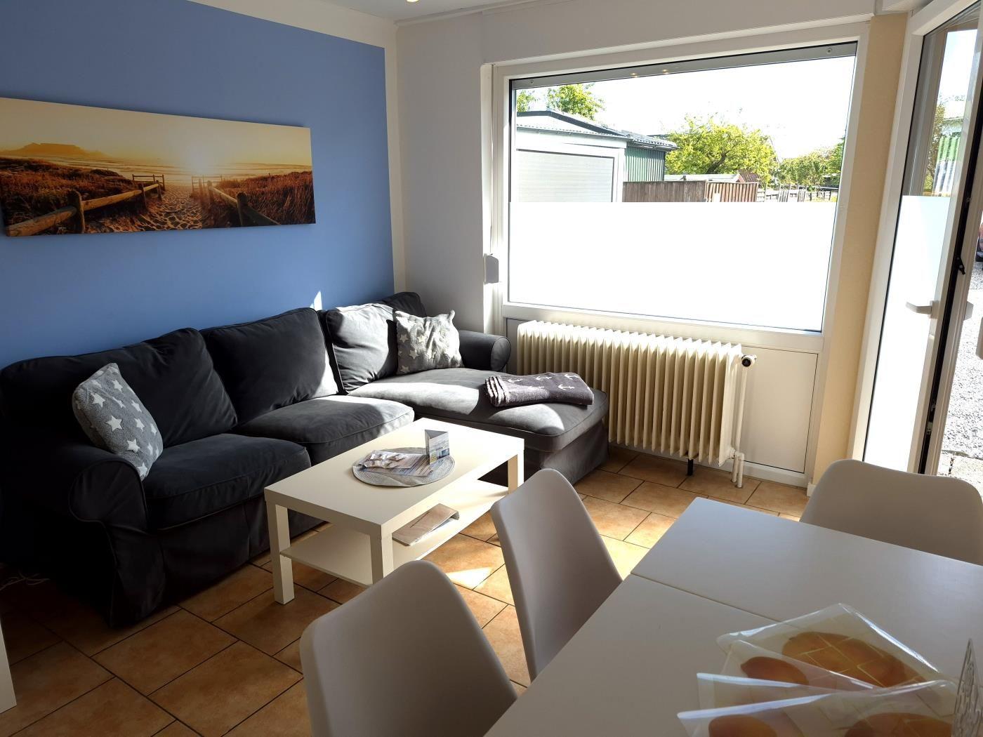 Wohn- und Essbereich mit Sofa, Tisch und Stühlen. Wandbild und Fenster zur Außenseite.