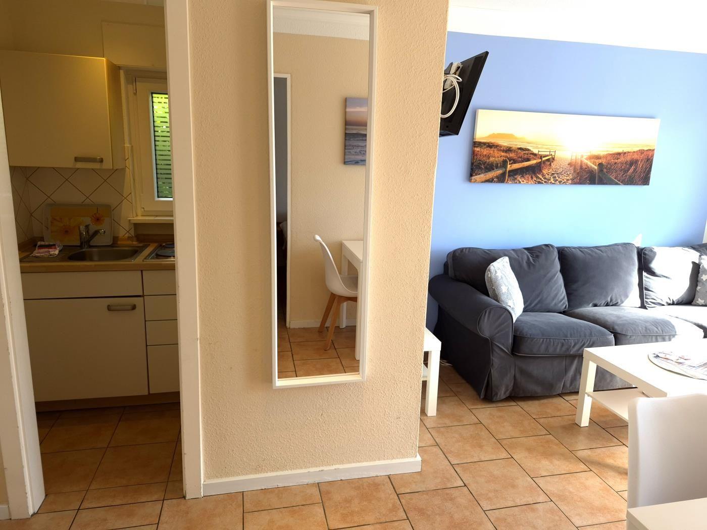 Wohnzimmer mit Sofa, Fernseher und Küchenbereich im Hintergrund.