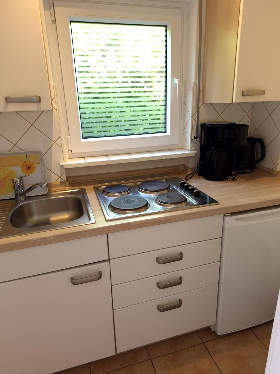 Küche mit Herd, Spüle und Fenster. Auf der Arbeitsplatte steht eine Kaffeemaschine.