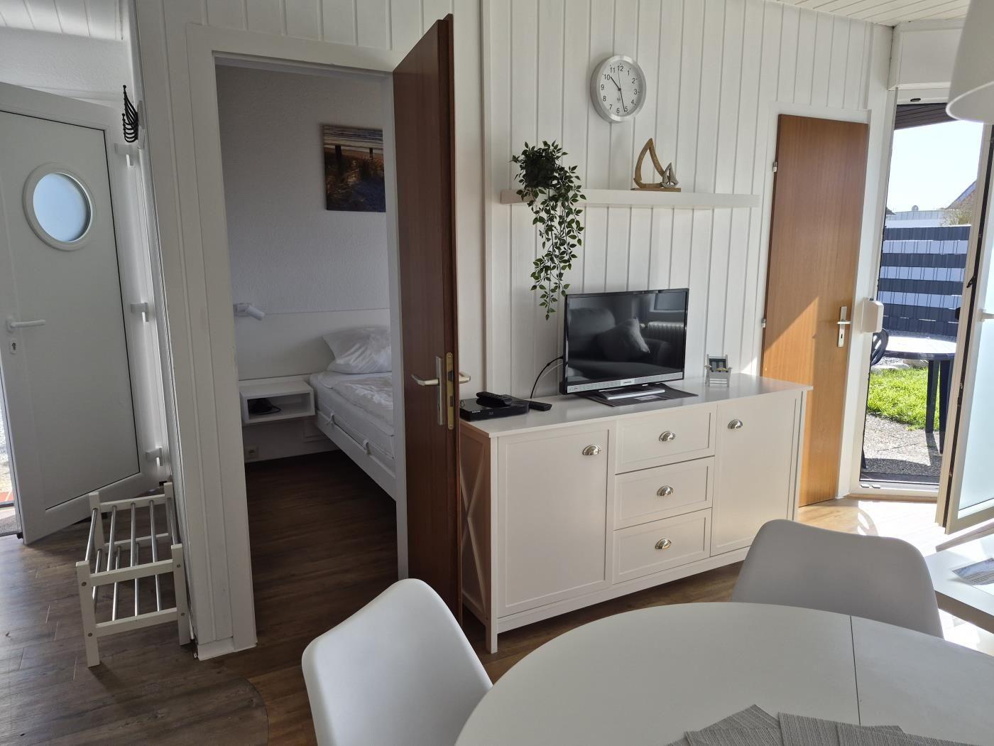 Wohnbereich mit TV-Schrank, Schlafzimmer und Terrasse. Holzboden und weiße Wände.
