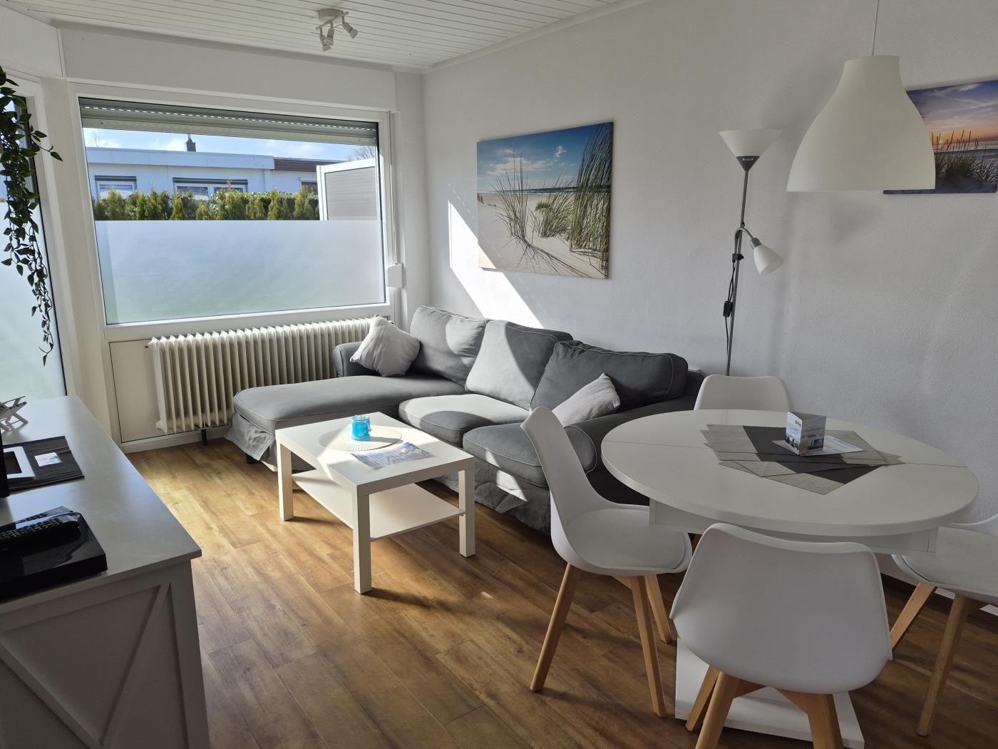 Wohn- und Essbereich mit grauem Sofa, runden Tisch und Holzboden.
