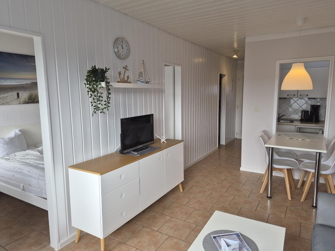 Wohn- und Essbereich mit TV, Schlafzimmer und Küche im Hintergrund.