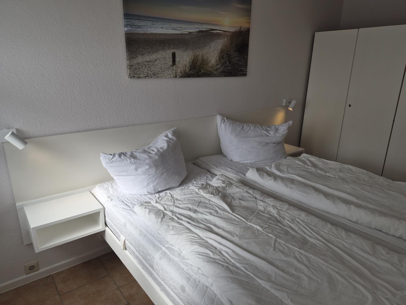 Schlafzimmer mit Bett, Nachttisch und Wandbild. Hintergrund ist ein Schrank.