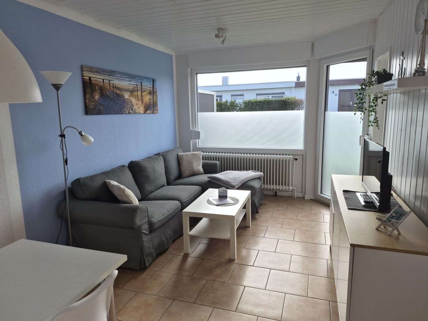 Wohnzimmer mit Sofa, Couchtisch und Fenster. Wandbild und Stehlampe sichtbar.