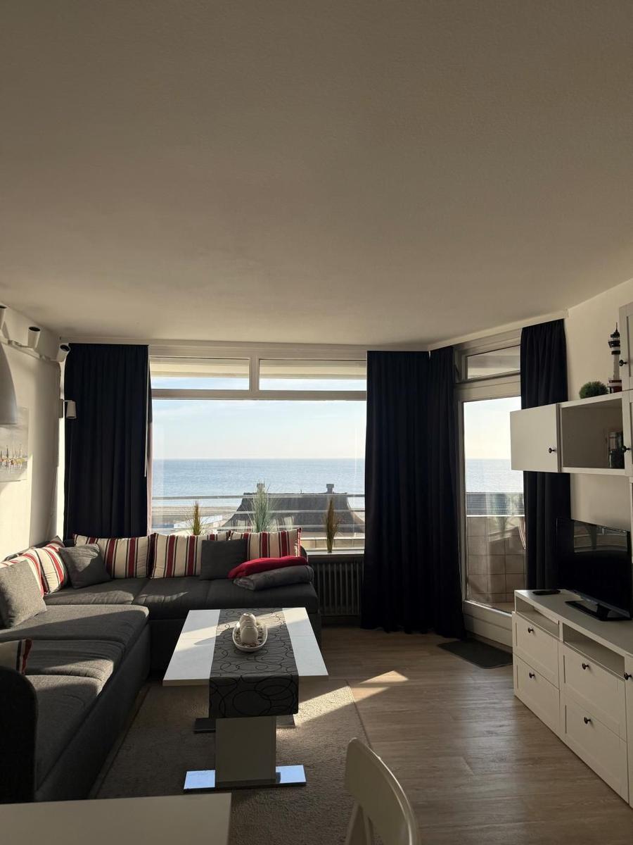 Wohnzimmer mit Sofa, Tisch und Blick aufs Meer durch große Fenster.