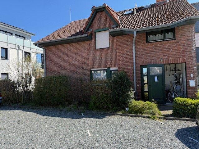 Zweistöckiges Backsteinhaus mit Dachfenster und grünem Eingang. Vor dem Haus liegt ein Kiesplatz.