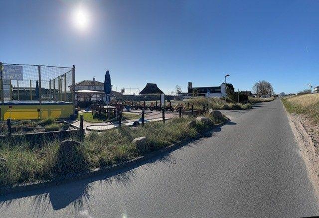 Asphaltierte Straße mit Sicht auf Terrasse, Grillbereich und Gebäude im Hintergrund.