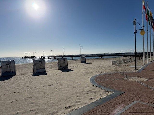 Strand mit Liegestühlen und Steg unter blauem Himmel.