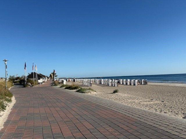 Pflasterweg entlang des Strandes mit Strandkörben und Meer im Hintergrund.