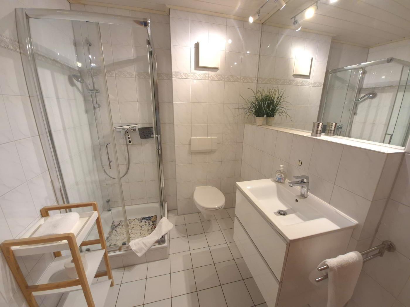 Badezimmer mit Dusche, WC und Waschbecken. Weiße Fliesen und Spiegel.