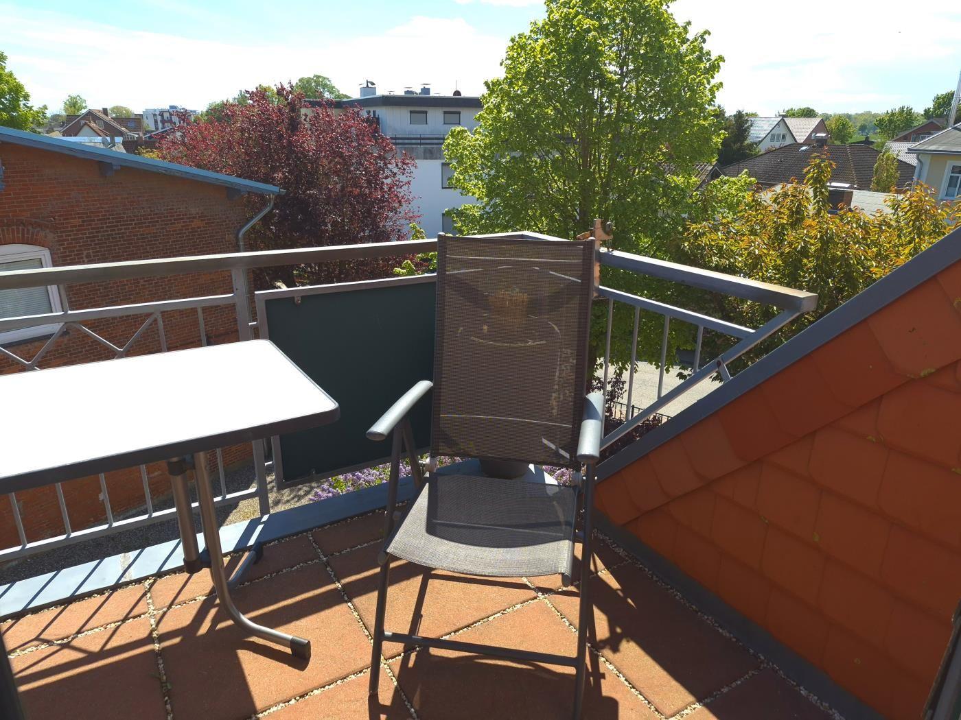 Terrasse mit Tisch und Stuhl, Blick auf Wohnhäuser und Bäume.