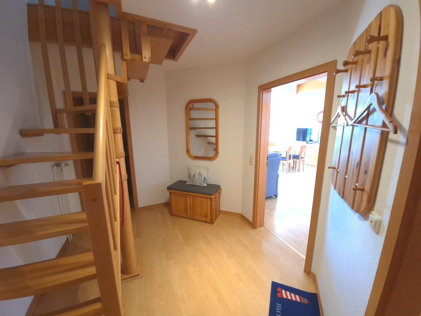 Eingangsbereich mit Holztreppe, Kleiderständer und Sitzbank.