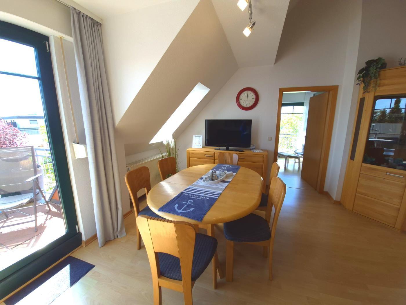 Esszimmer mit runder Tisch, Stühlen und TV unter Dachschrägen.