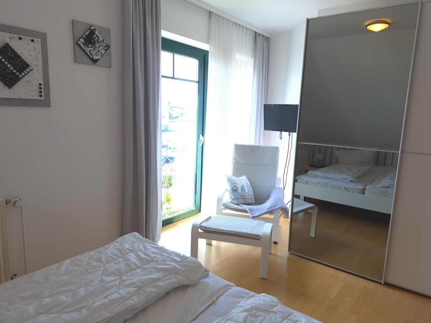 Schlafzimmer mit Bett, Spiegel und Tür zum Balkon.
