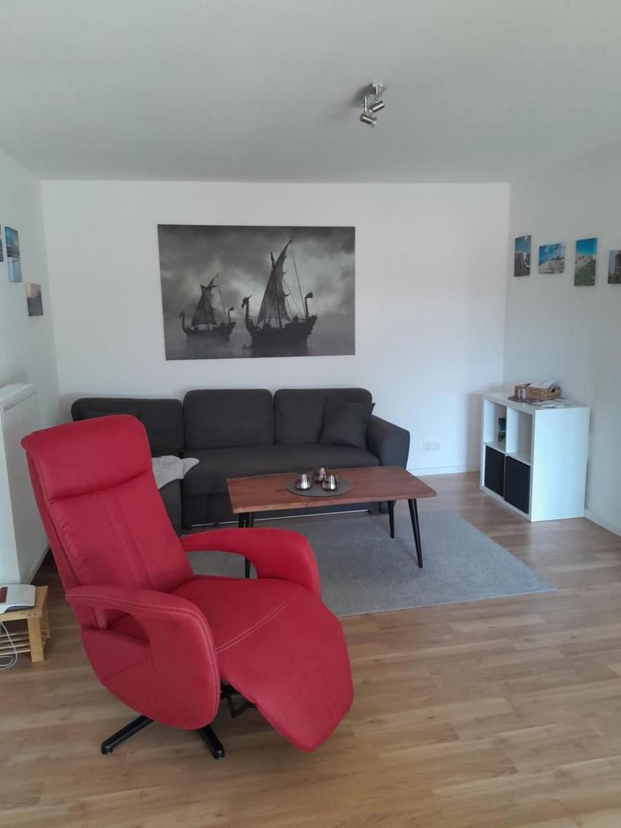 Ein Wohnzimmer mit grauem Sofa, rotem Sessel und Holzboden.