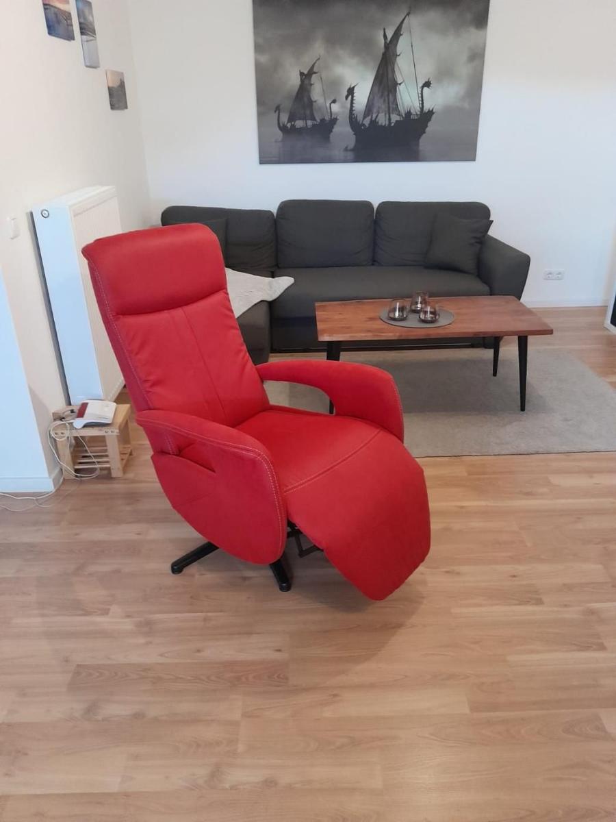 Rotes Sessel, graue Couch, Holztisch, Wandbild mit Schiffen.