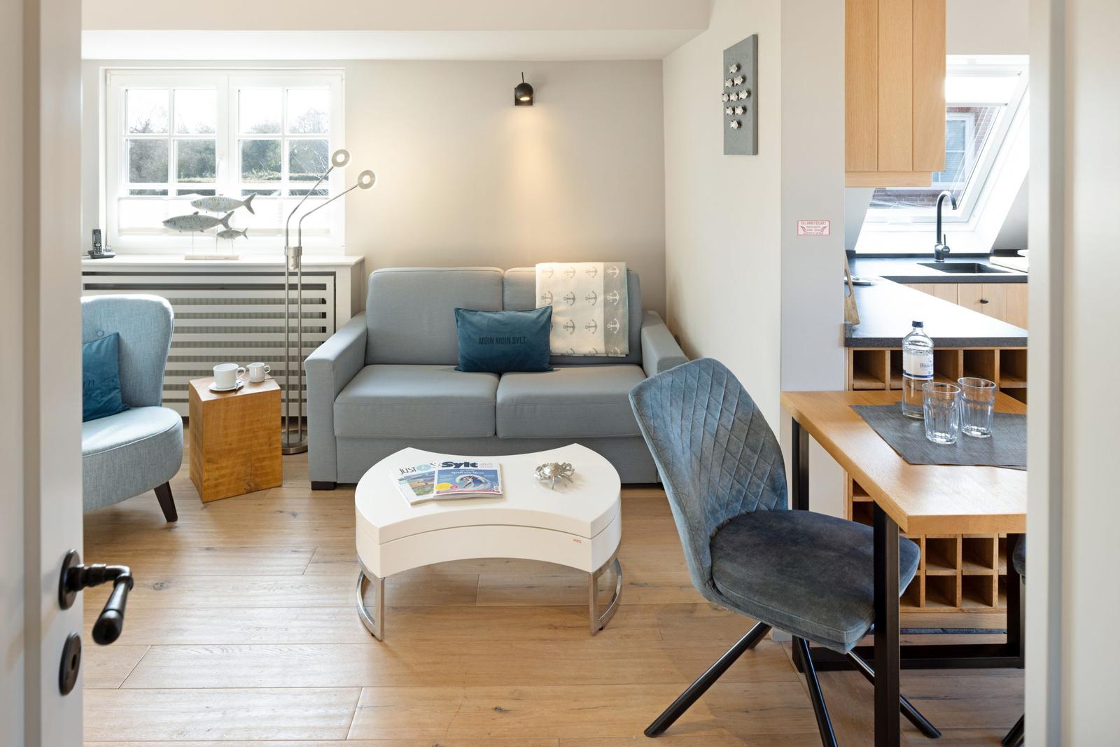 Wohnzimmer mit Sofa, Sessel und Esstisch. Küche mit Dachfenster sichtbar.