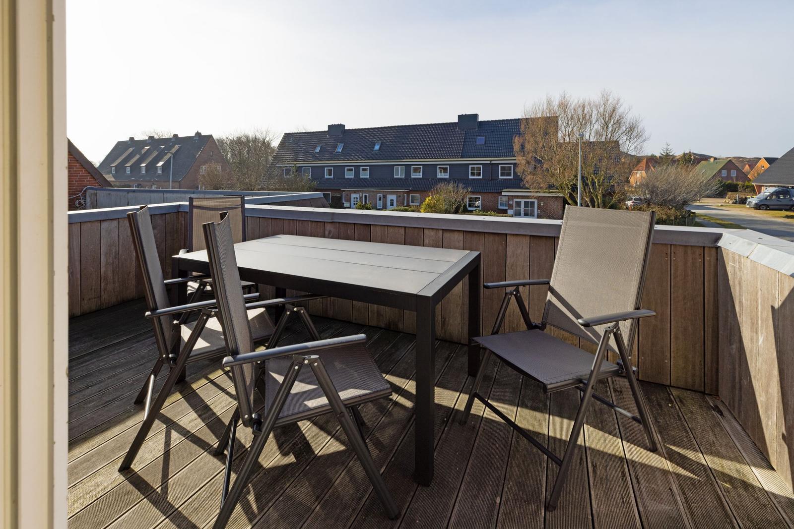Terrasse mit Tisch und Stühlen. Holzgeländer und Blick auf Wohnhäuser.