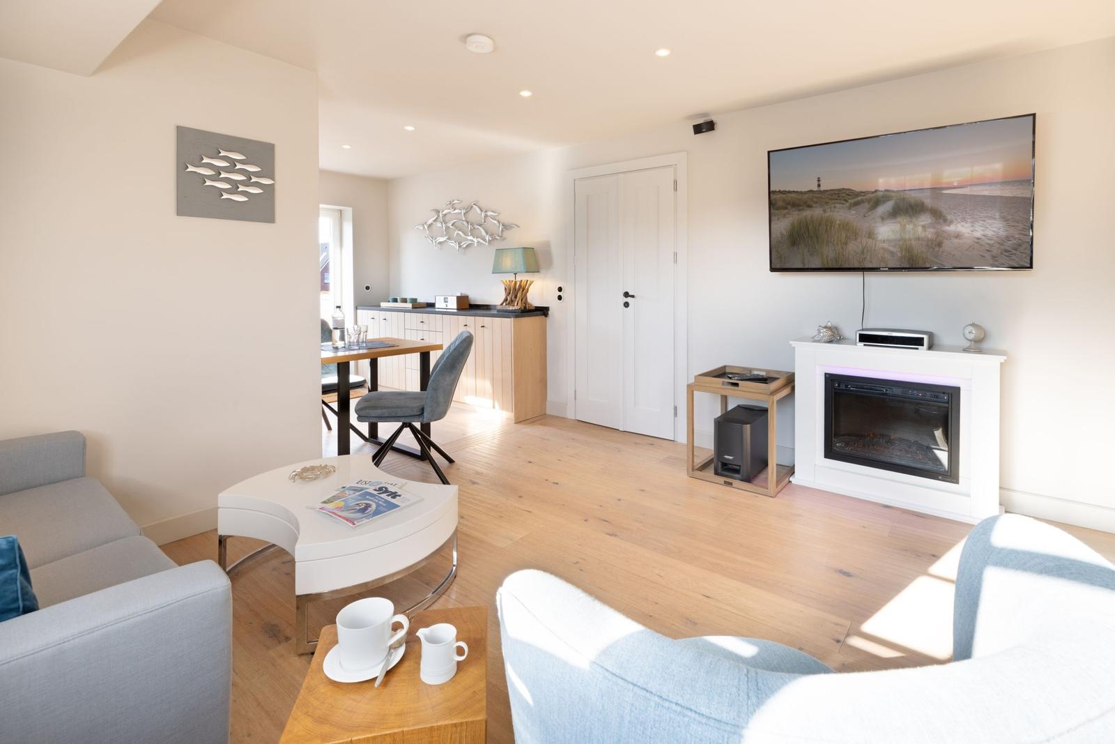 Wohnzimmer mit Sofa, Fernseher und Kaminofen. Essbereich im Hintergrund.