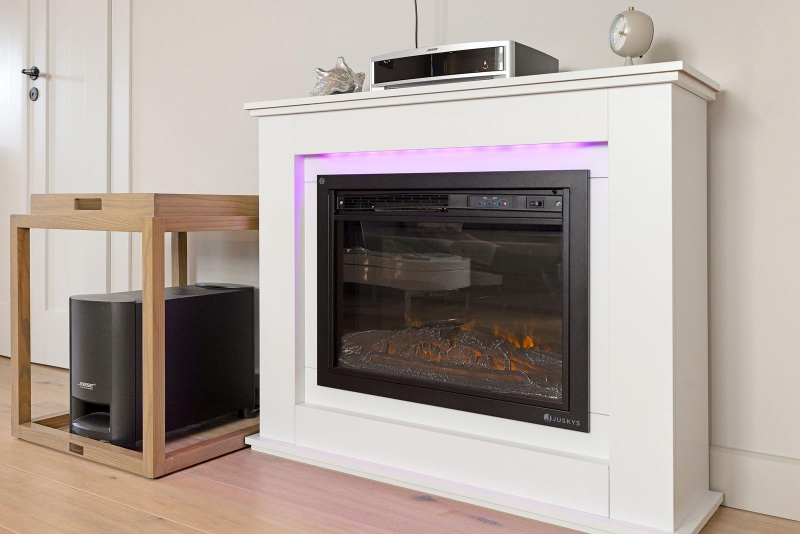 Ein elektrischer Kamin mit lila Beleuchtung und einem Bose Lautsprecher auf einem Holzgestell.