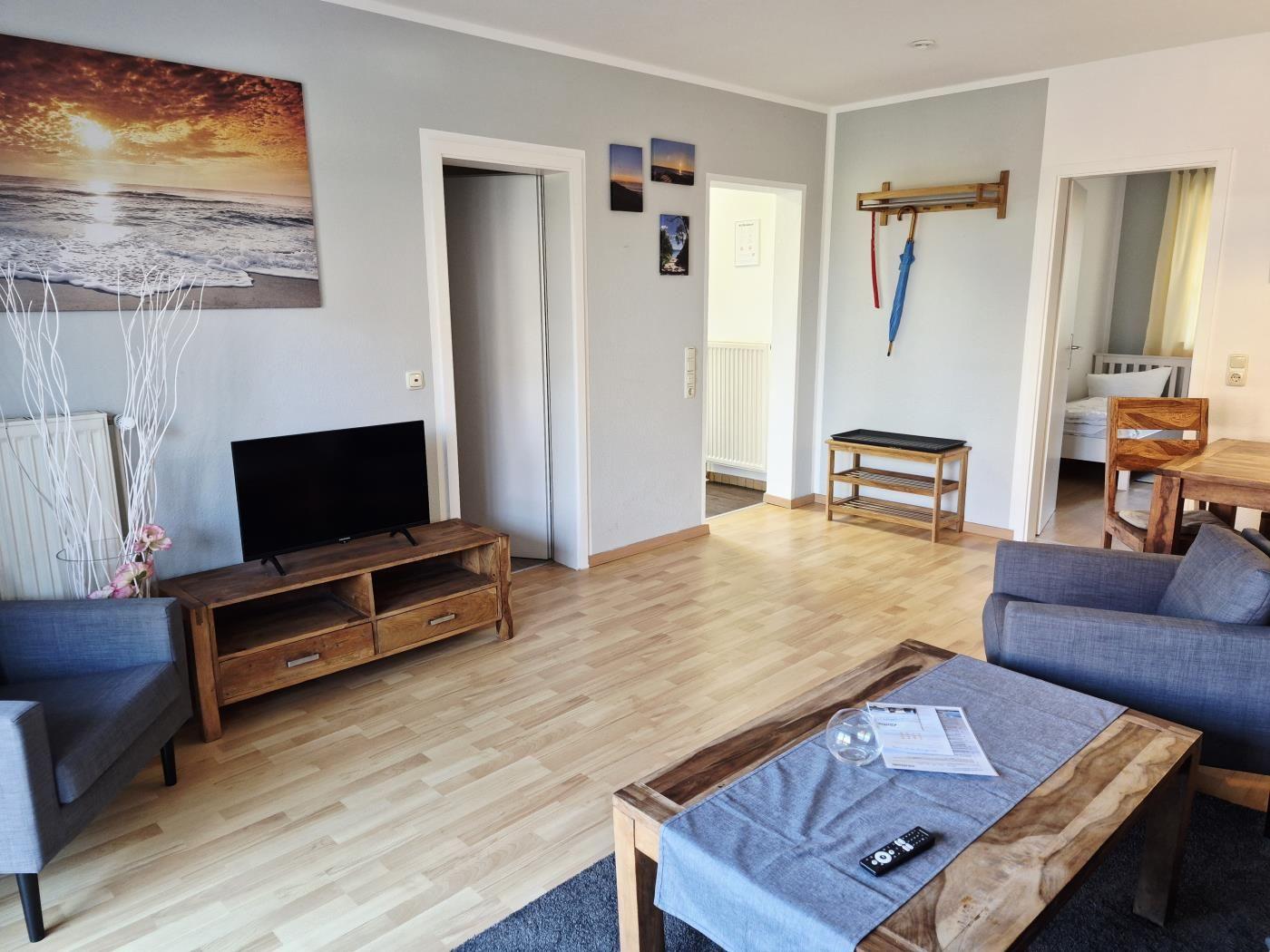 Wohnzimmer mit TV, Sofa, Tisch und Blick in Schlafzimmer.