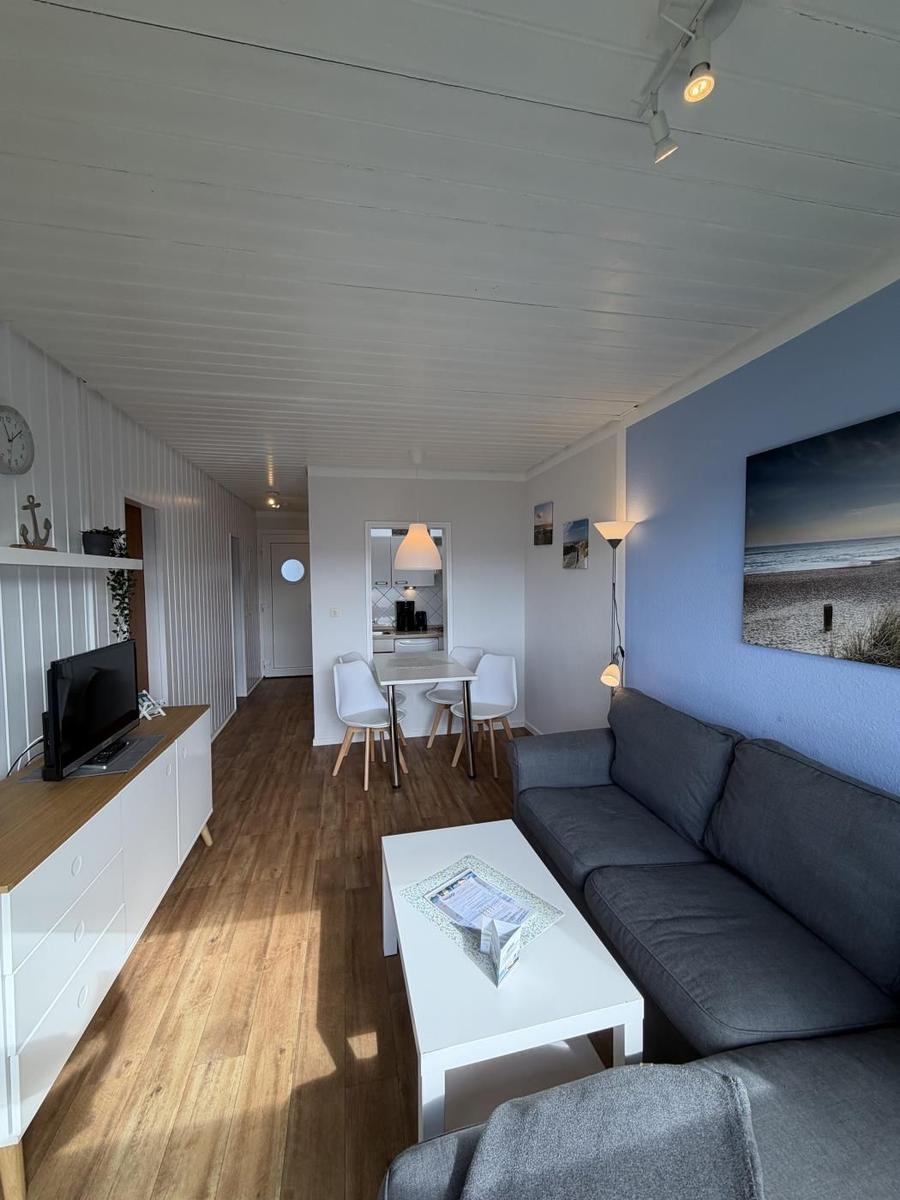 Wohnbereich mit Sofa, Esstisch und Küche im Hintergrund.
