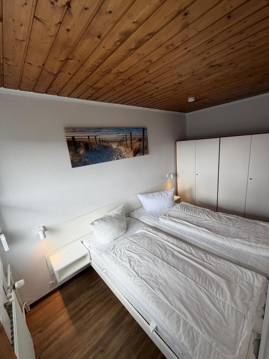 Schlafzimmer mit Doppelbett, Holzdecke und Kleiderschrank. Wandbild zeigt Strand.