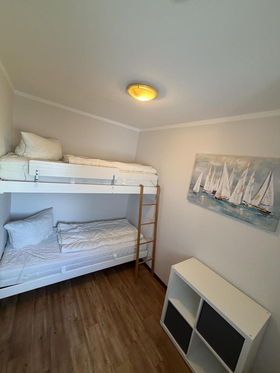 Zimmer mit Doppelstockbett, Holzboden und Wandbild mit Segelbooten.