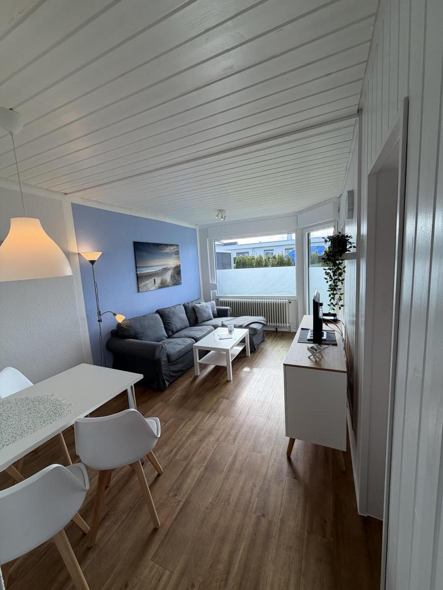 Wohn- und Essbereich mit Sofa, Tisch und Stühlen. Holzboden und weiße Wände.