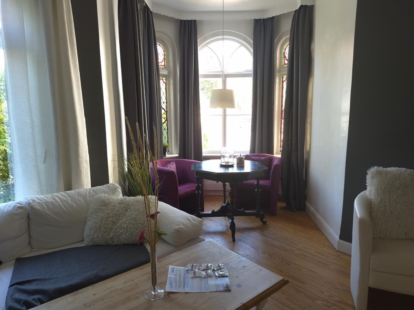 Ein Wohnzimmer mit Sofa, Stuhl und Tisch. Fenster mit Vorhängen und Holzboden.