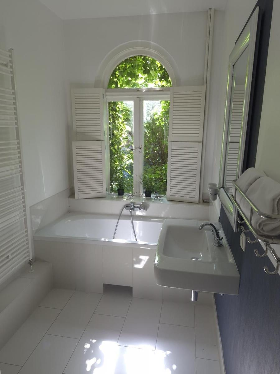 Badezimmer mit Badewanne, Waschbecken und Fenster mit Jalousien.