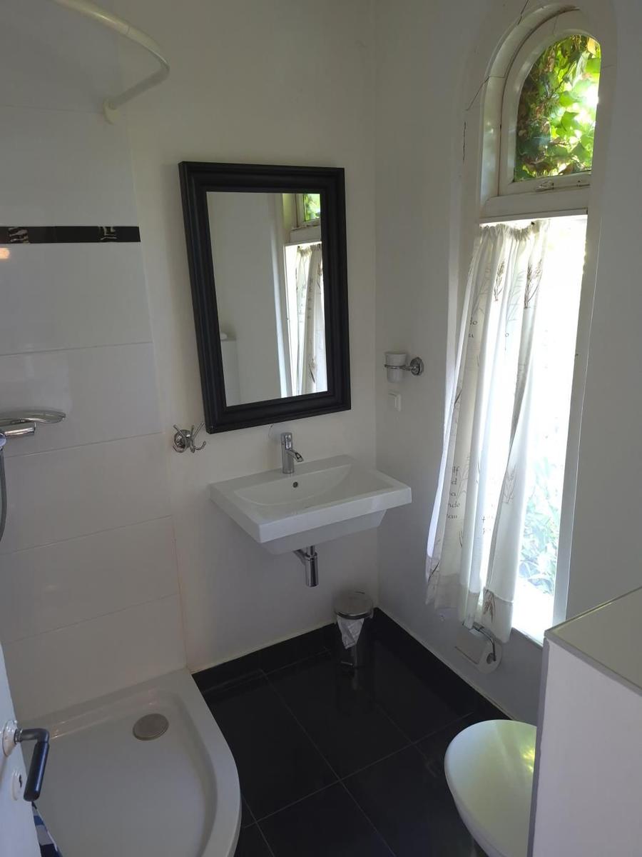 Badezimmer mit Waschbecken, Spiegel, Dusche und Fenster mit Vorhang.