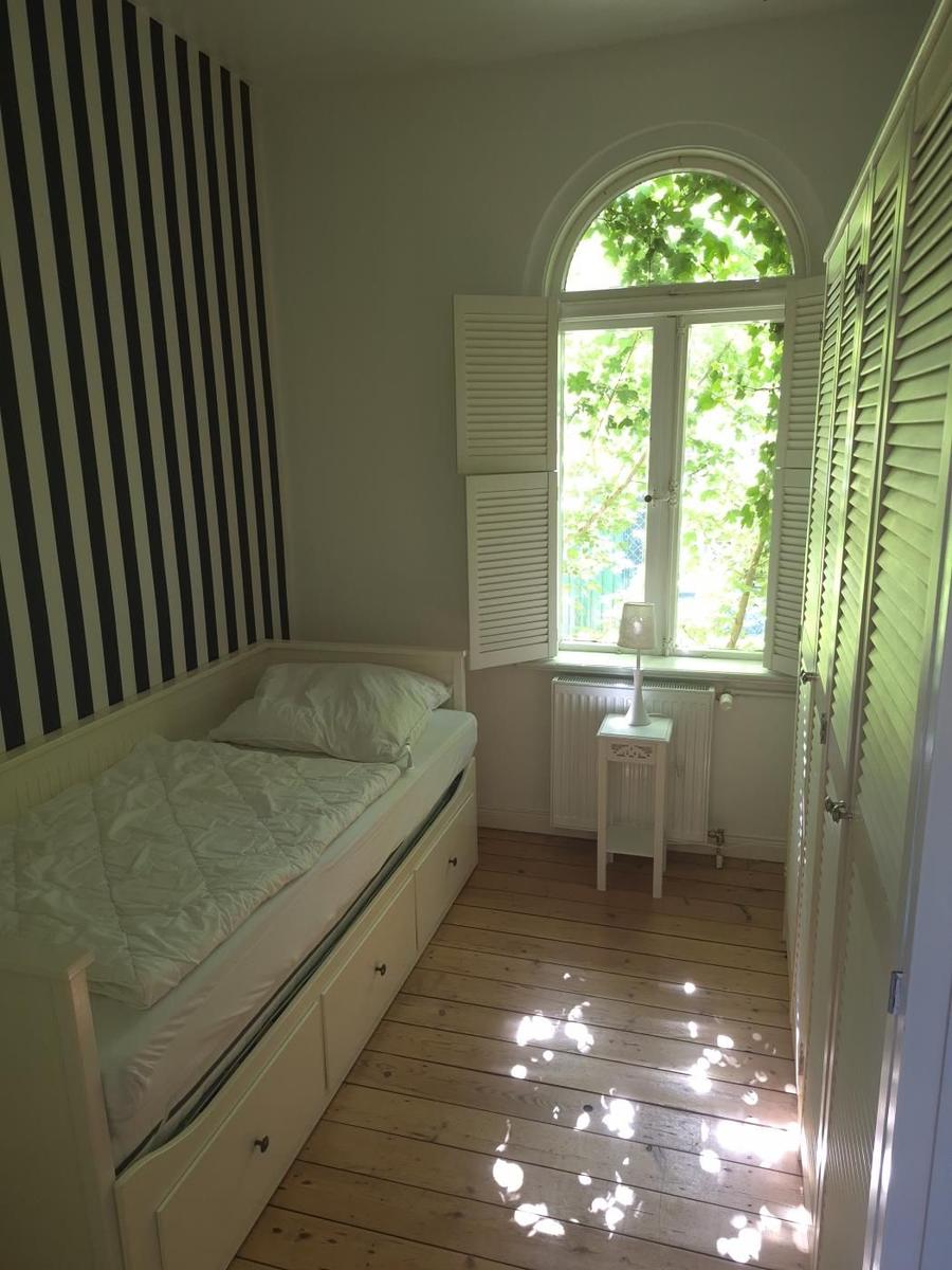 Schlafzimmer mit Bett, Holzboden und Bogenfenster mit weißen Jalousien.
