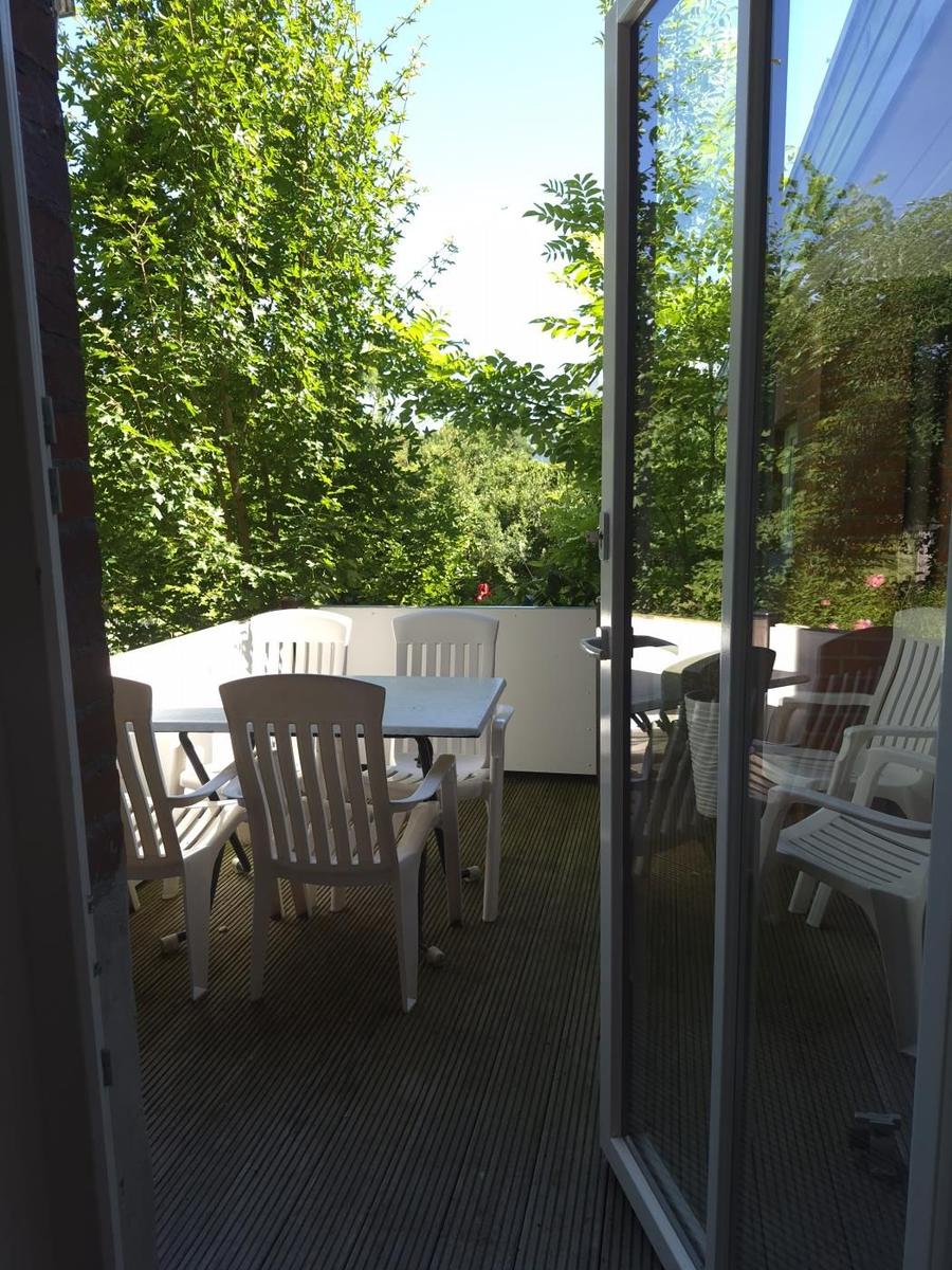 Terrasse mit weißem Tisch und Stühlen, umgeben von grünen Bäumen.