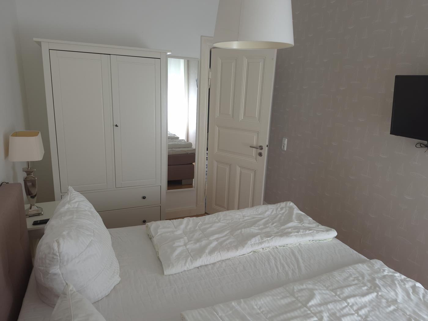 Schlafzimmer mit weißem Bett, Kleiderschrank und Wand-TV